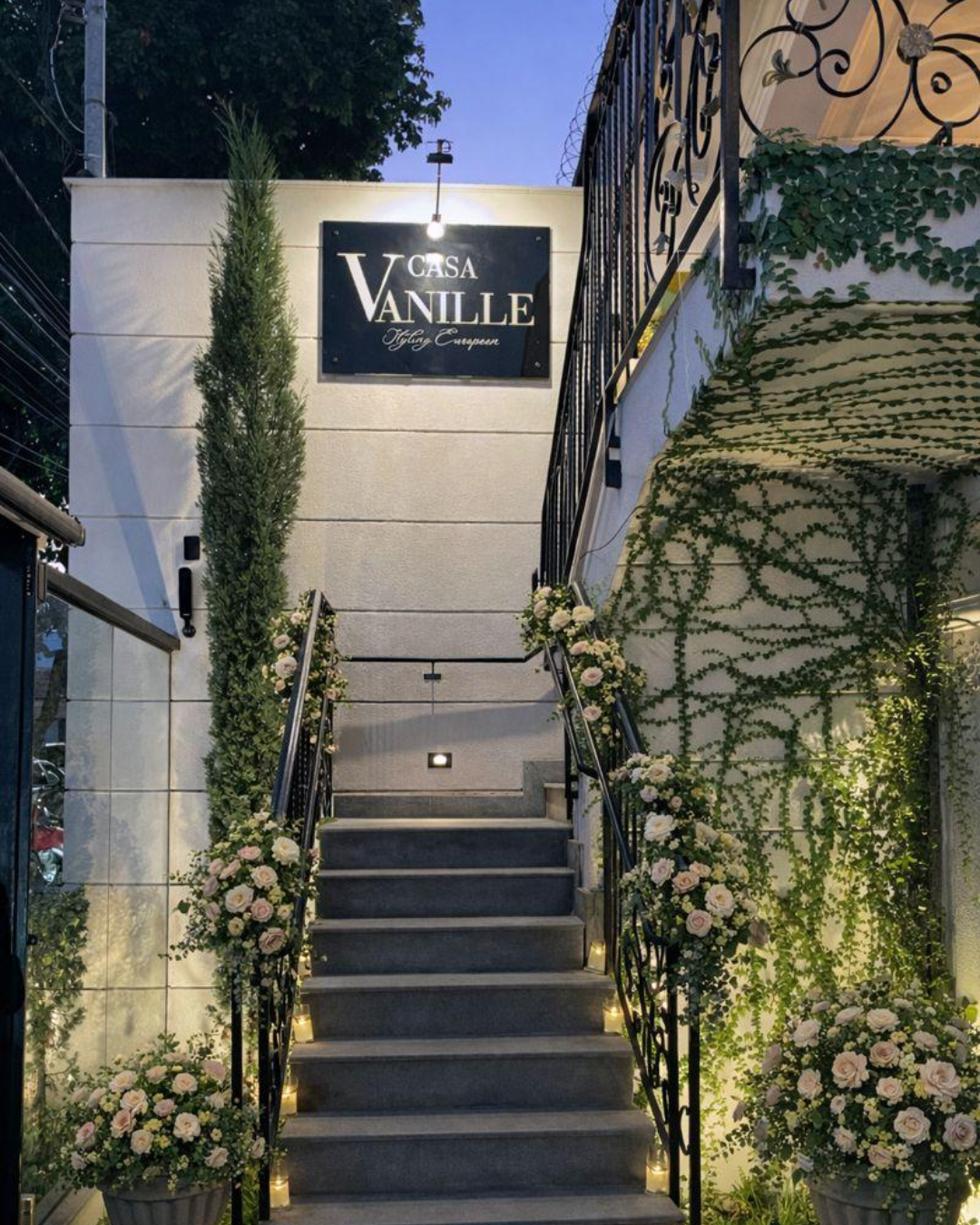 Entrada da Casa Vanille com escadaria florida e letreiro iluminado